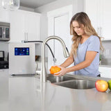 Woman washing orange at kitchen sink with hydrogen water machine on counter