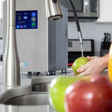 Hydrogen water machine on kitchen counter as person washes green apple at sink